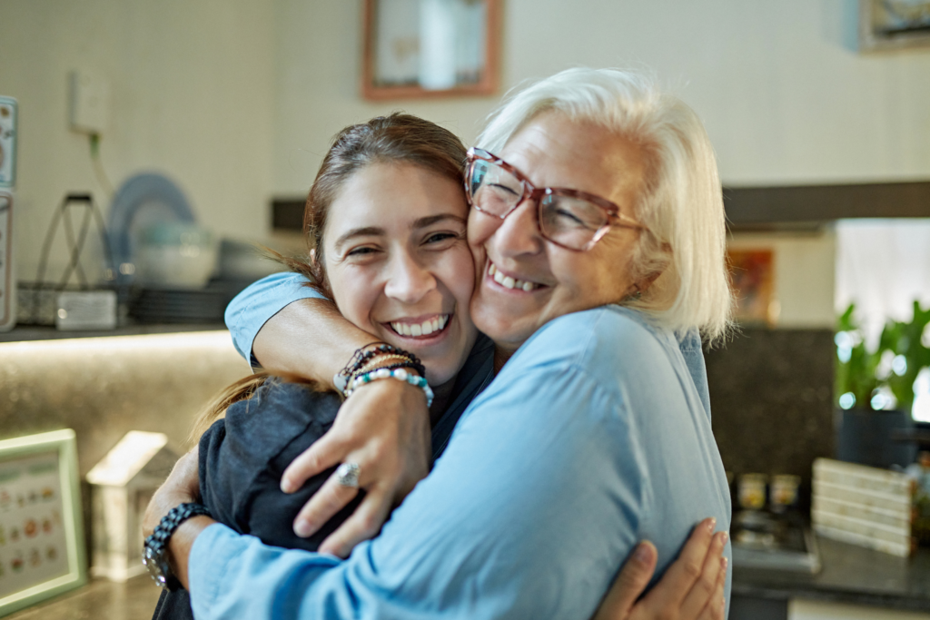 Photo of an older and younger woman smiling and hugging one another.