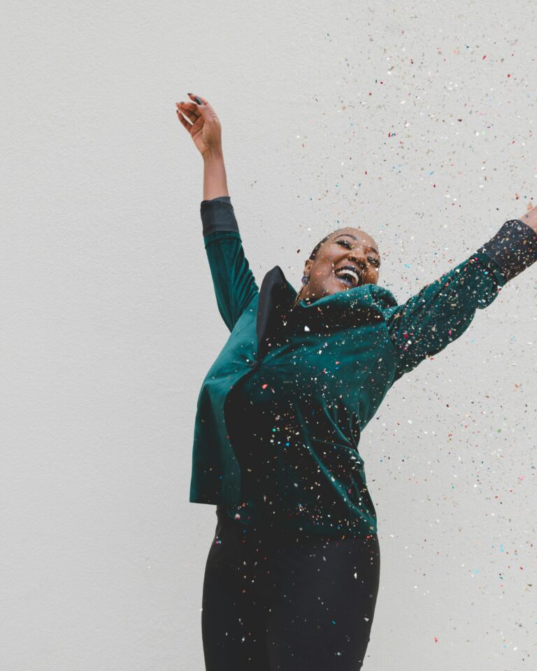 woman smiling with arms raised and glitter falling