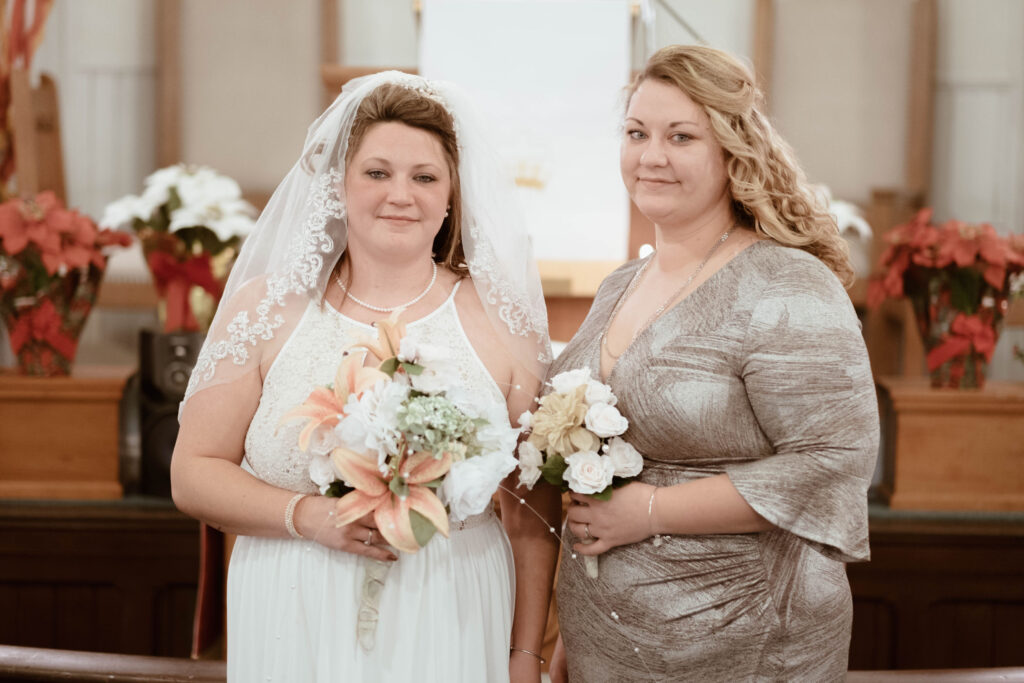 Rachel and Lauren hold bouquets. One of them is wearing a white dress and veil.