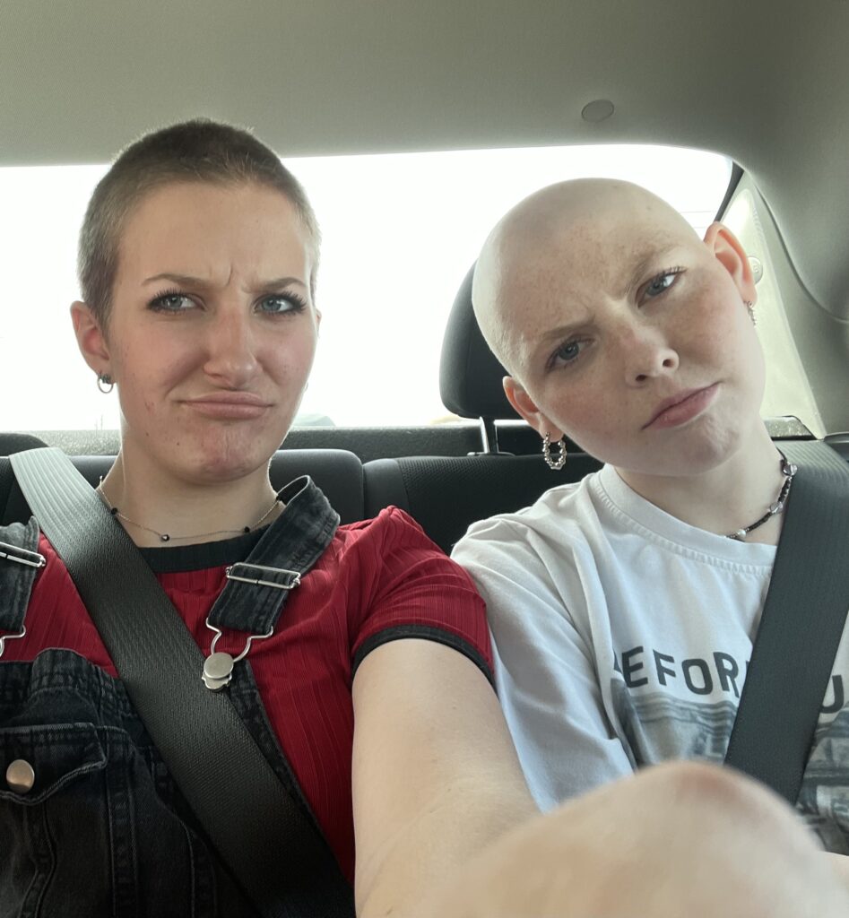 Zaytey and Lilian make silly faces in the backseat of a car, both with shaved heads