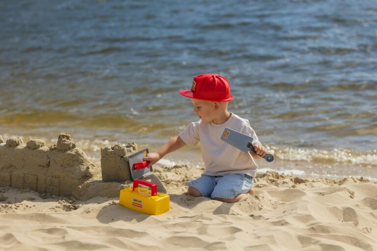 little boy in a red hat making a sandcastle on a beahc
