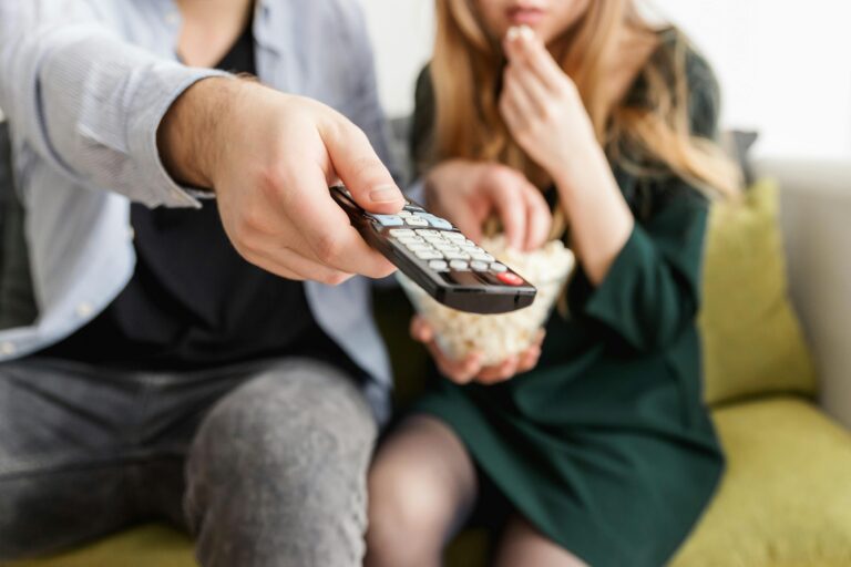 man holding a remote sitting next to a woman eating popcorn on the couch