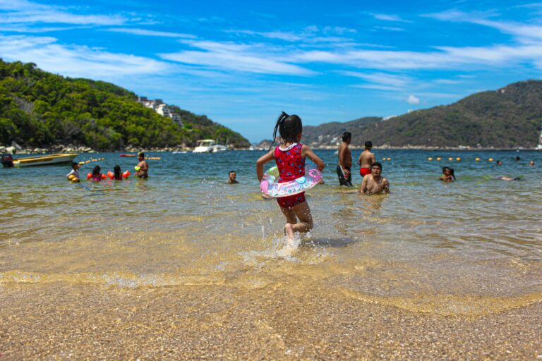 kids and families playing and swimming in clear blue water on a rocky beach