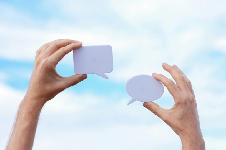white man's hands holding up paper cut outs of speech bubbles in front of a blue cloudy sky