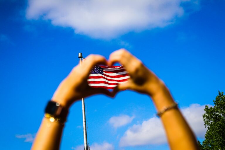 person holding their hands in the shape of a heart in front of the American flag