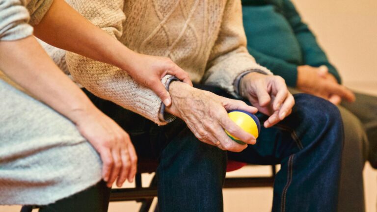 younger person touching the forearm of an older person who is holding a stress ball. Image is meant to convey the idea of helping someone