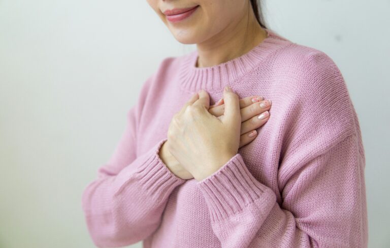 women in pink sweater putting her hands on her heart in a gesture of gratitude